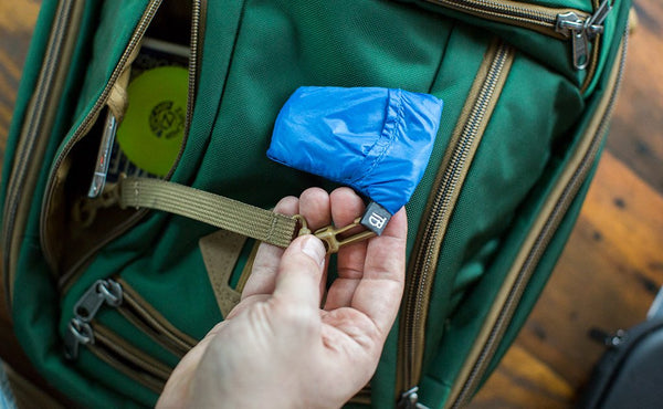 A person lashing a pocket travel pillow to the Synik 22 using the included 8" Coyote (brown) Key Strap.